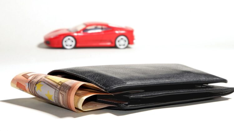 Wallet with money sticking out in front of a red sedan.